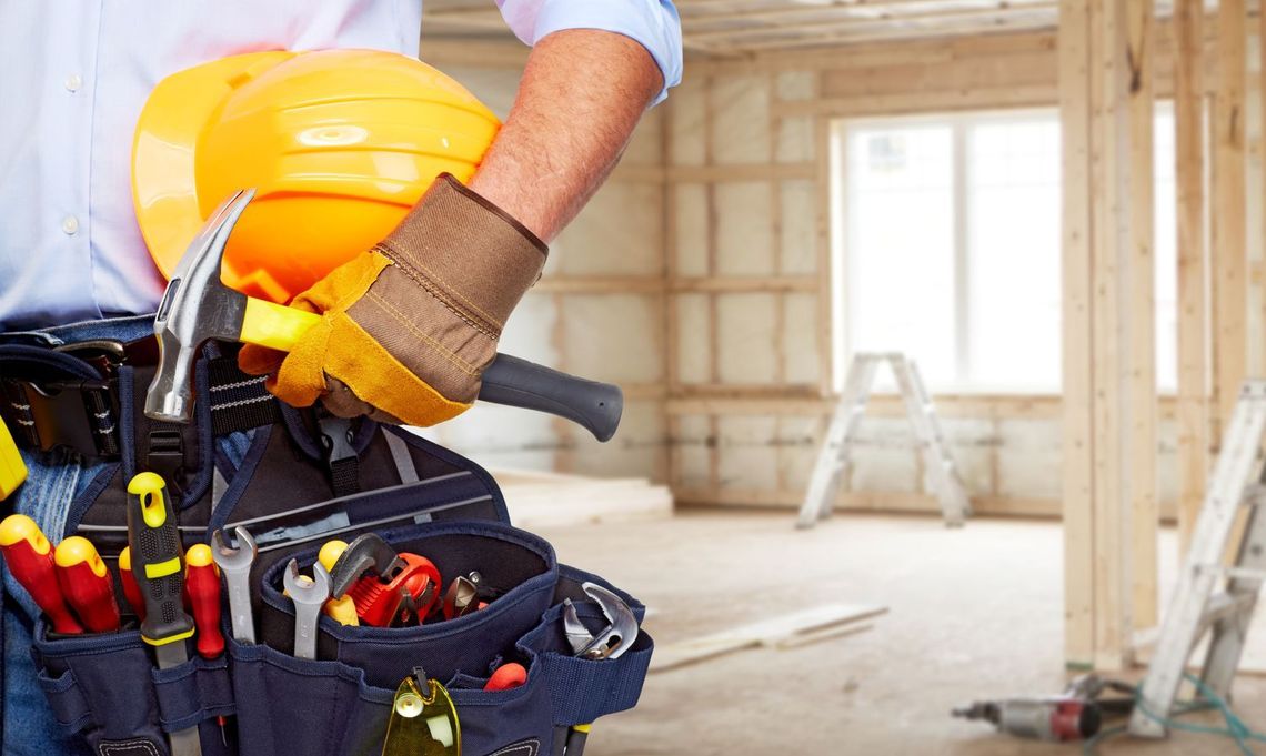 A construction worker is wearing a hard hat , gloves , a hammer , and a tool belt.