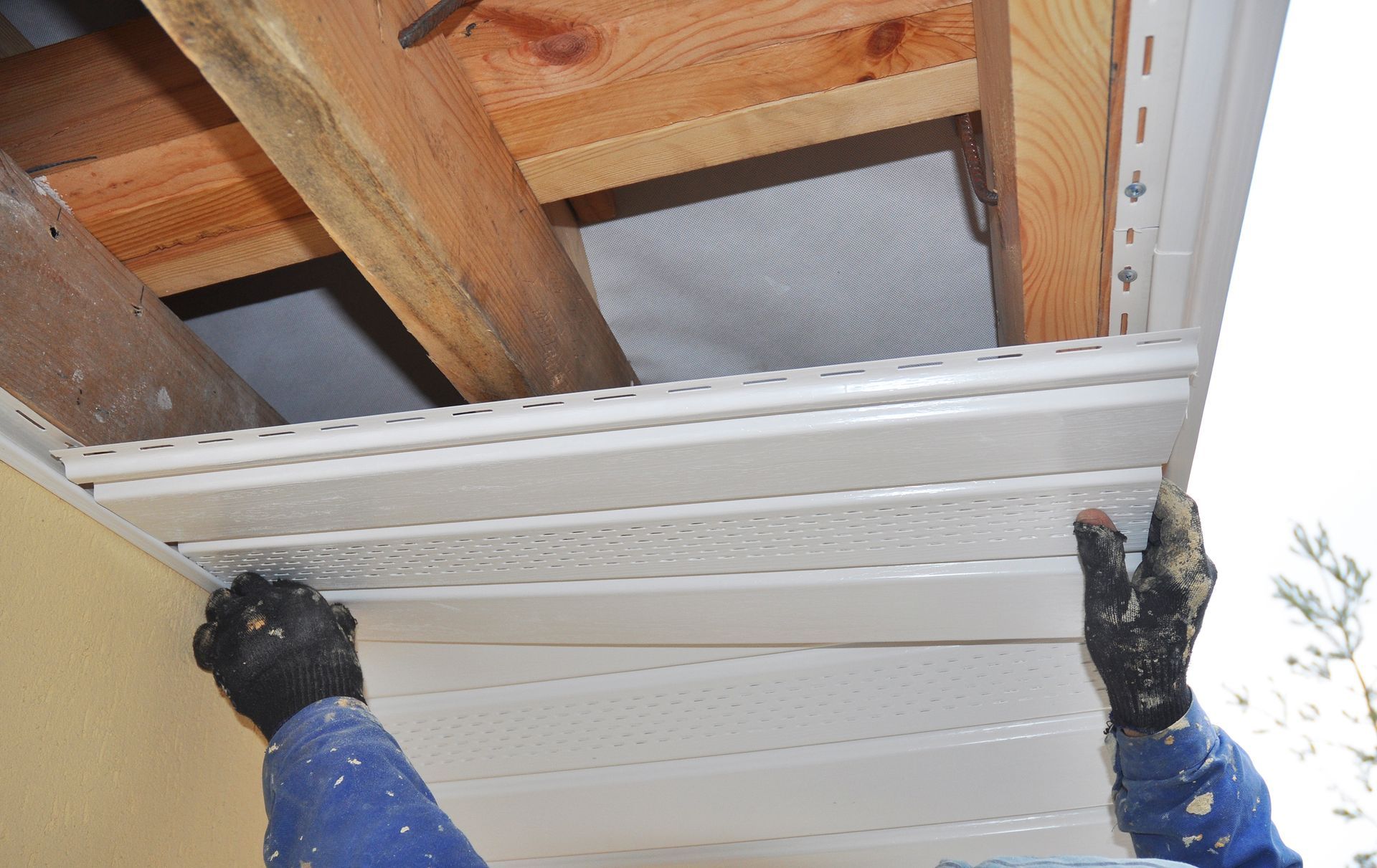 A person is installing siding on the side of a house.