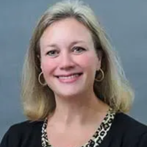 Blonde woman with a slight smile, wearing a black top with animal print trim.
