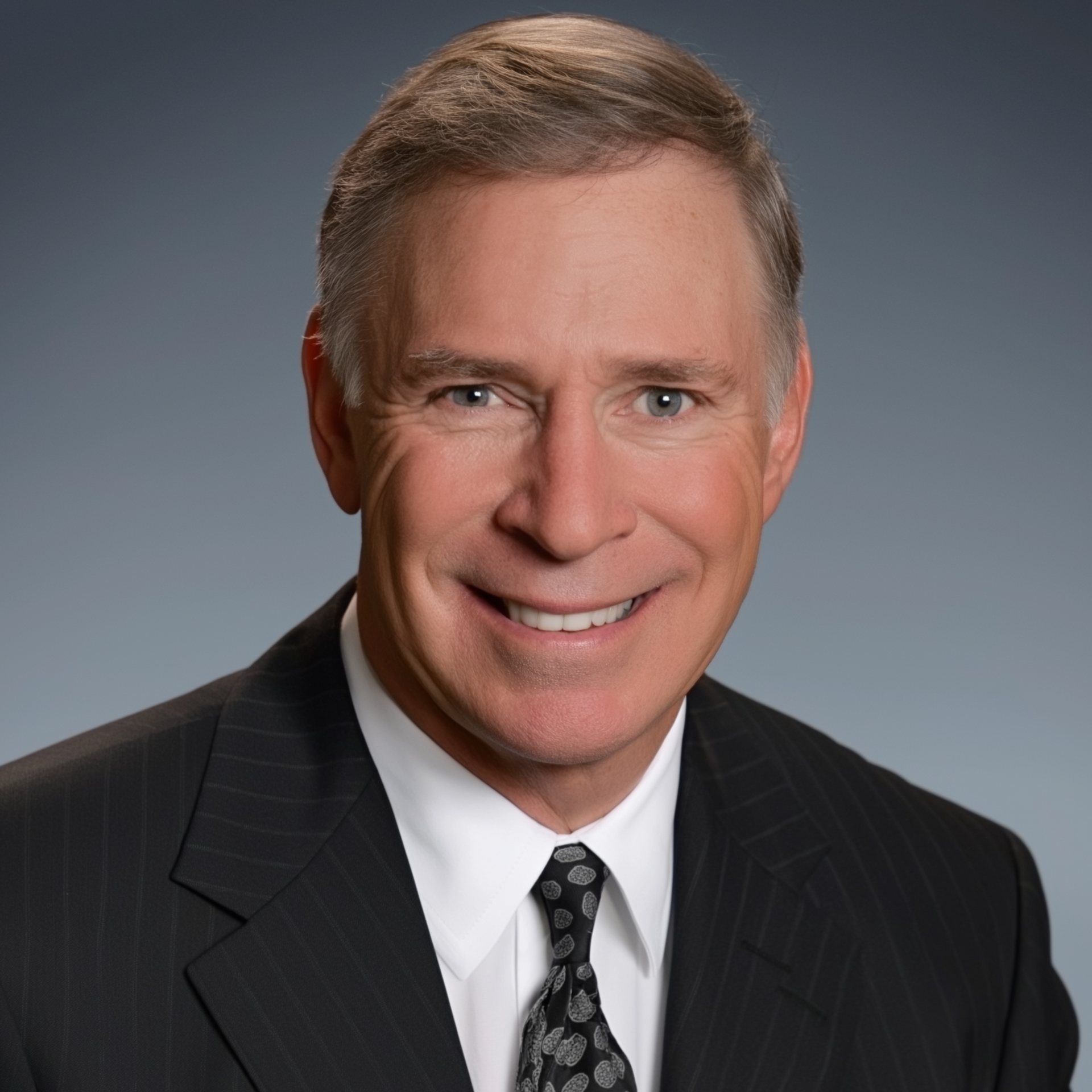 Smiling man in a suit and tie, against a dark blue background.