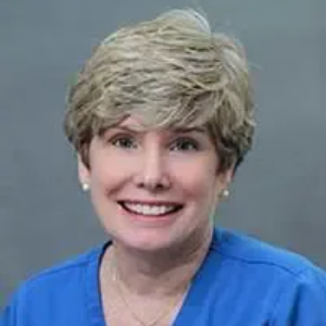 Woman with short blonde hair smiles, wearing a blue top.