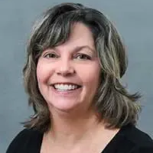 Woman with brown wavy hair smiling at camera, wearing a black top.
