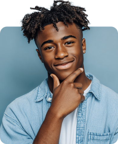 Young Black man with locs, smiling, hand on chin, in a denim shirt, against a blue background.
