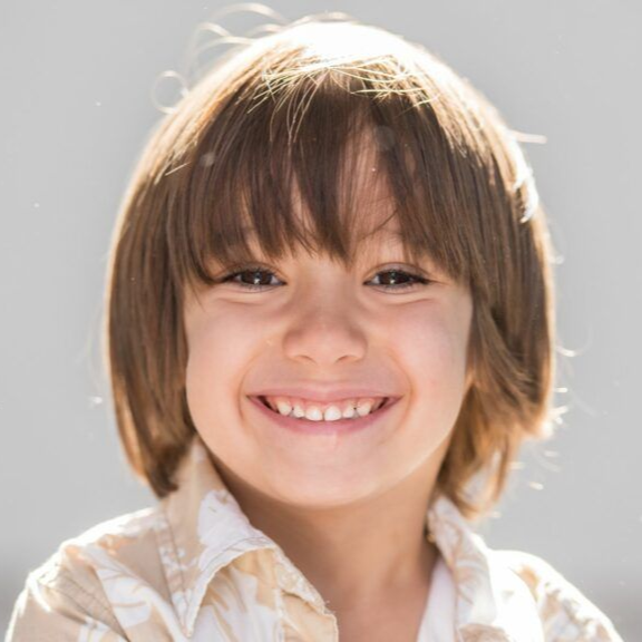 Smiling child with brown hair and bangs, wearing a light-colored button-down shirt.