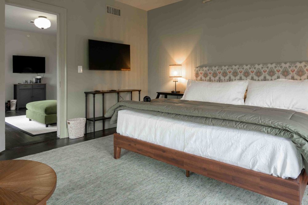 Bedroom with bed, television, open doorway to another room with seating.