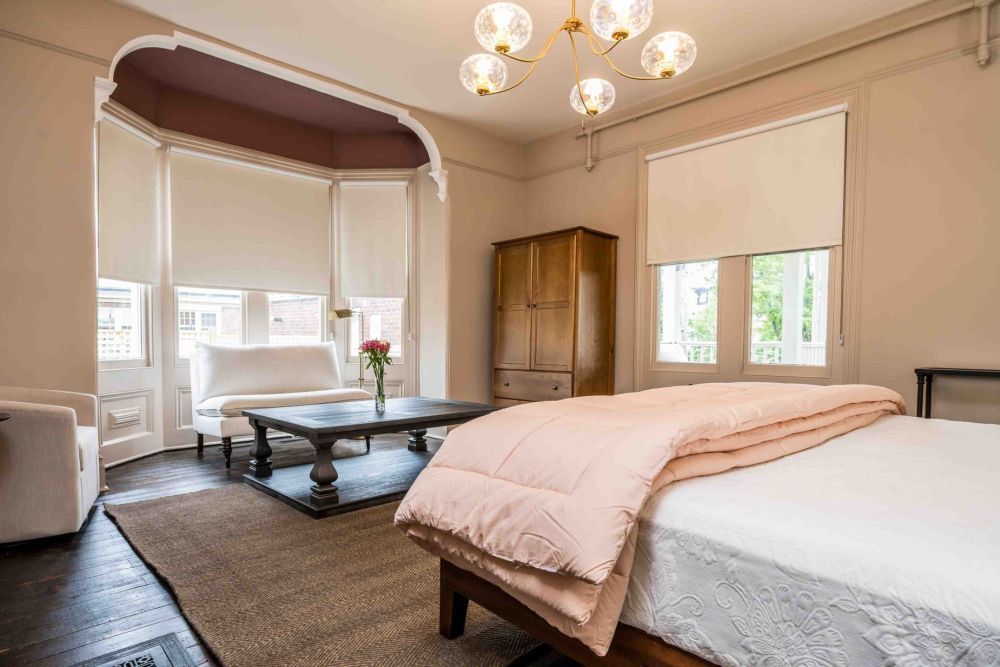 Bedroom with bed, seating area, and wooden wardrobe. Neutral color palette.