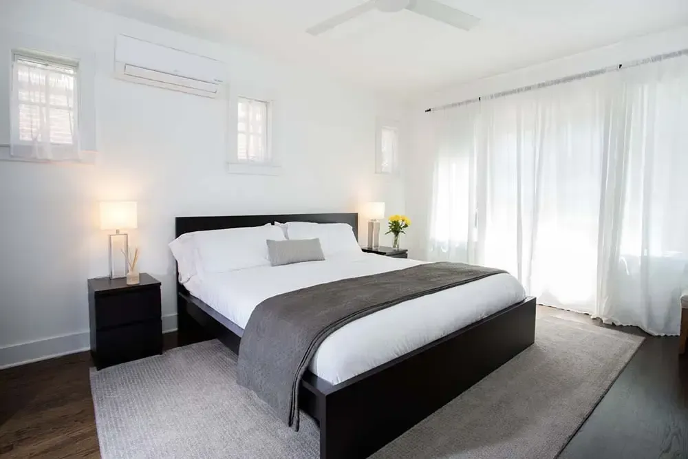 Modern white bedroom with a bed, nightstands, and sheer curtains.