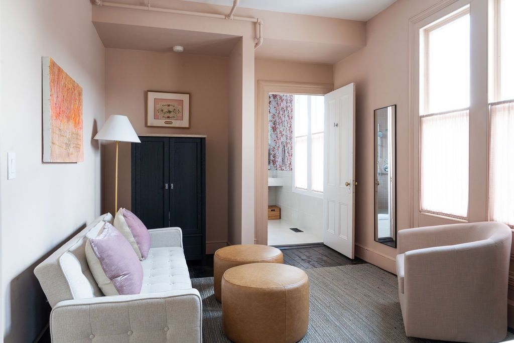 Cozy room with a white sofa, two round brown ottomans, and a closet. Open door reveals a bathroom.