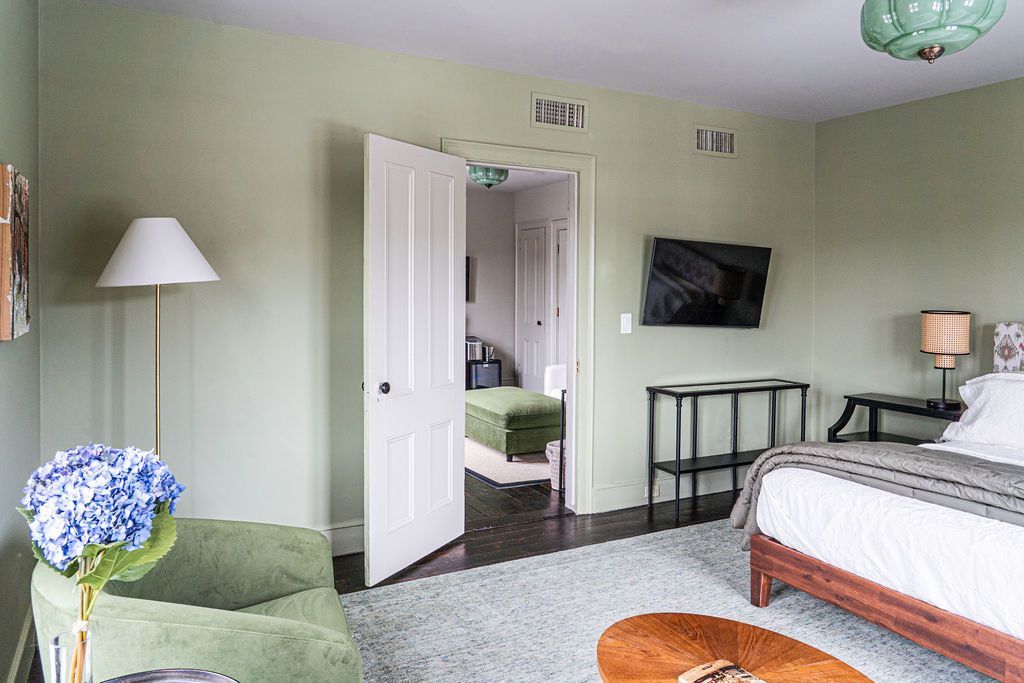 Bedroom with bed, television, open doorway to another room with seating.