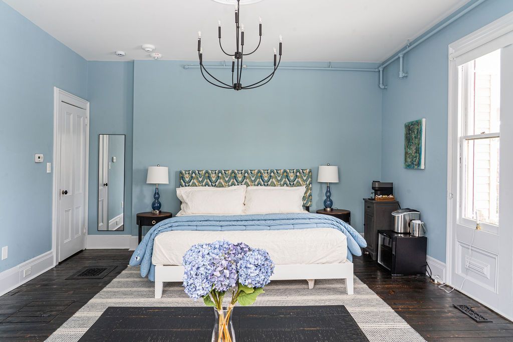 Bedroom with bed, blue blanket, armchairs, and bay window.