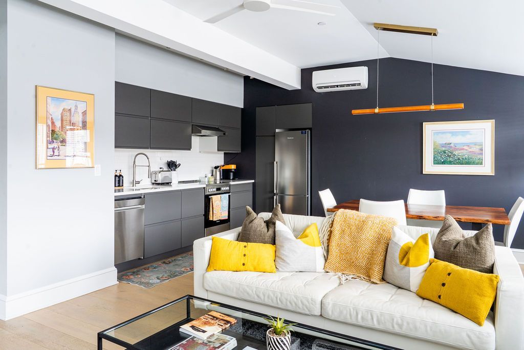 Modern living room with kitchen. Gray walls, white couch with yellow pillows.