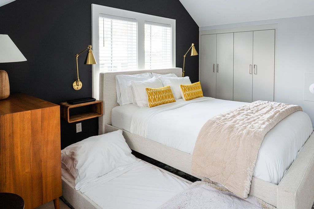 Bedroom with a bed, a pull-out bed, a dresser, dark wall, and gold sconces.