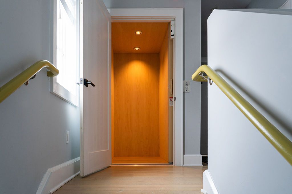 Open elevator door in a hallway, lined with orange wood. Yellow handrails and light-colored walls.