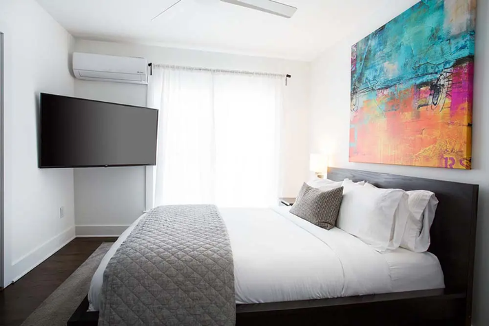 Bedroom with bed, large abstract art, TV, air conditioner, and bright window.