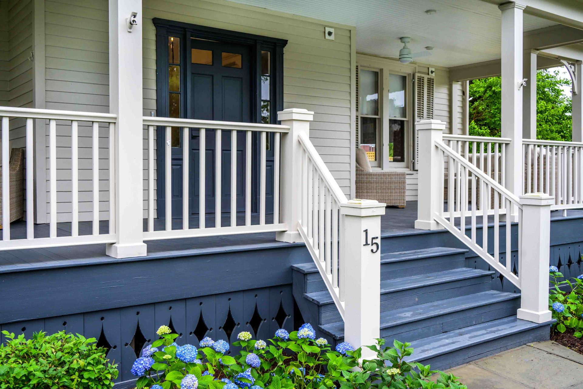 White porch with gray steps and blue door, number