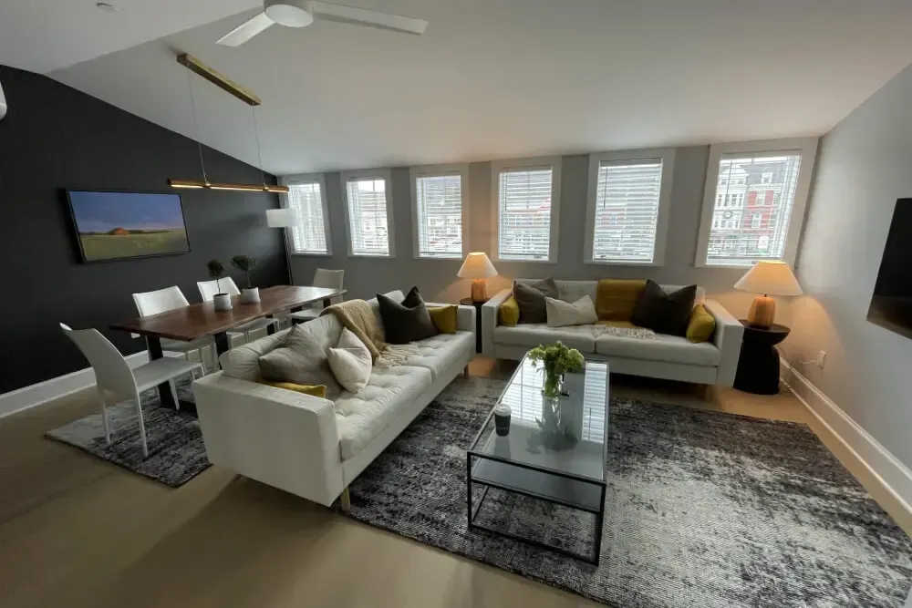 Modern living room with white sofas, dining table, and dark accent wall.