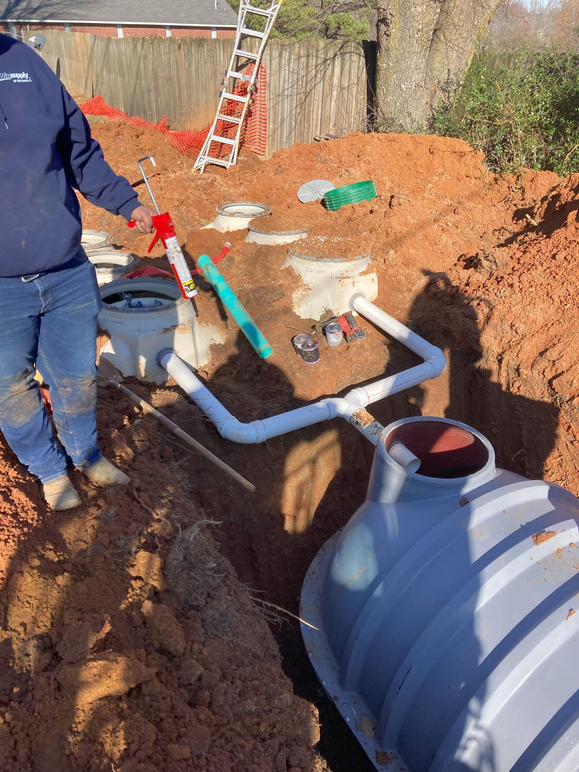 A man is standing in the dirt next to a septic tank.