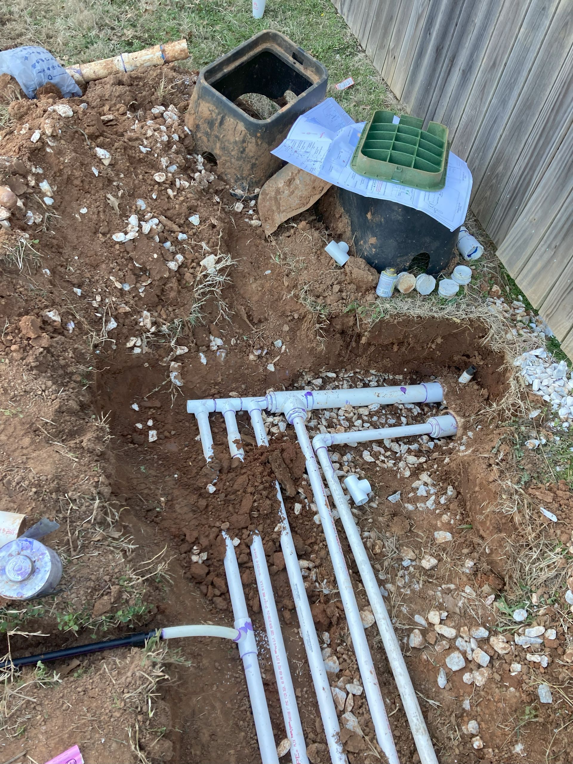 A bunch of pipes are laying in the dirt next to a fence.