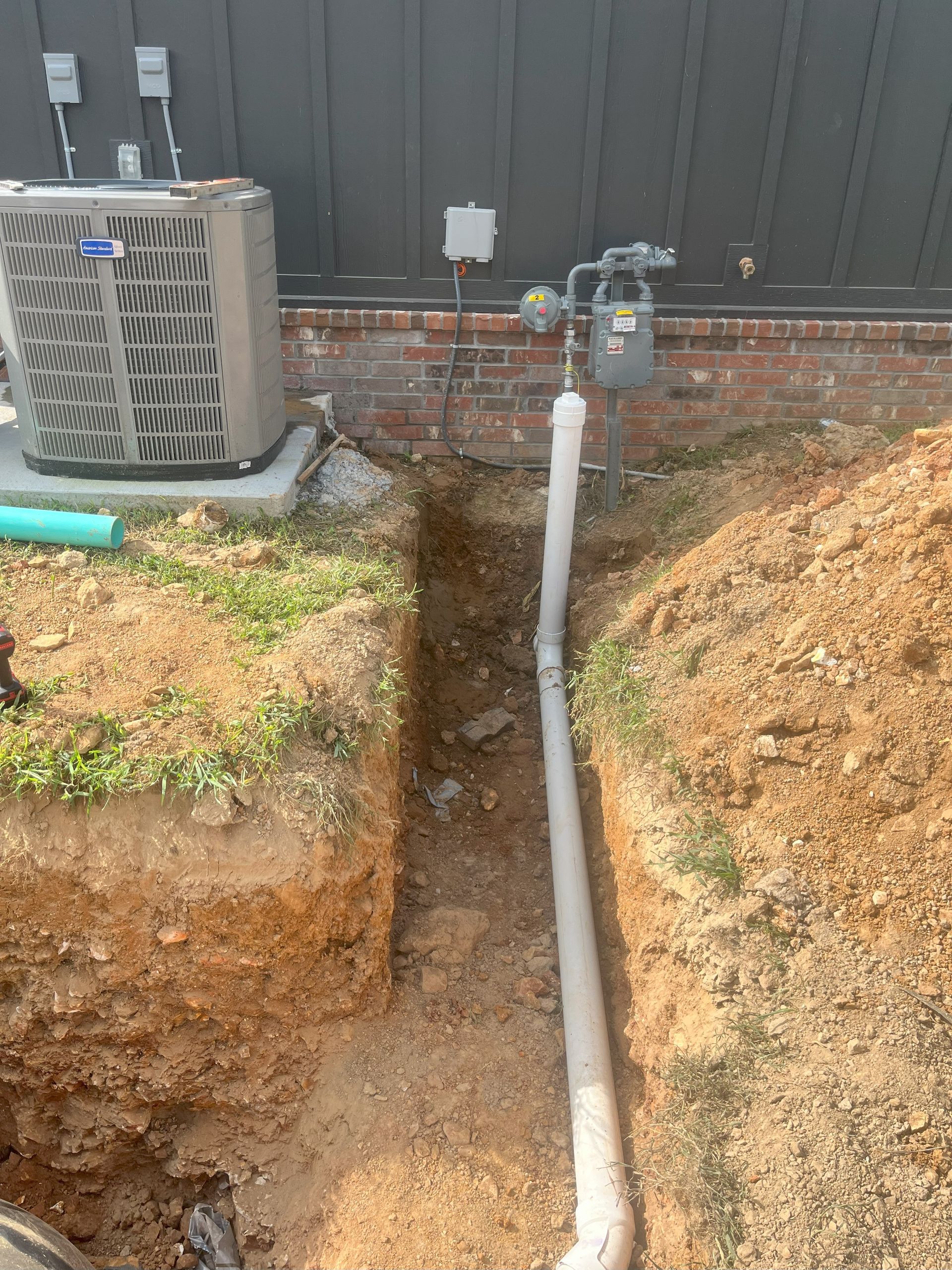 A drain pipe is being installed in a hole in the ground next to an air conditioner.