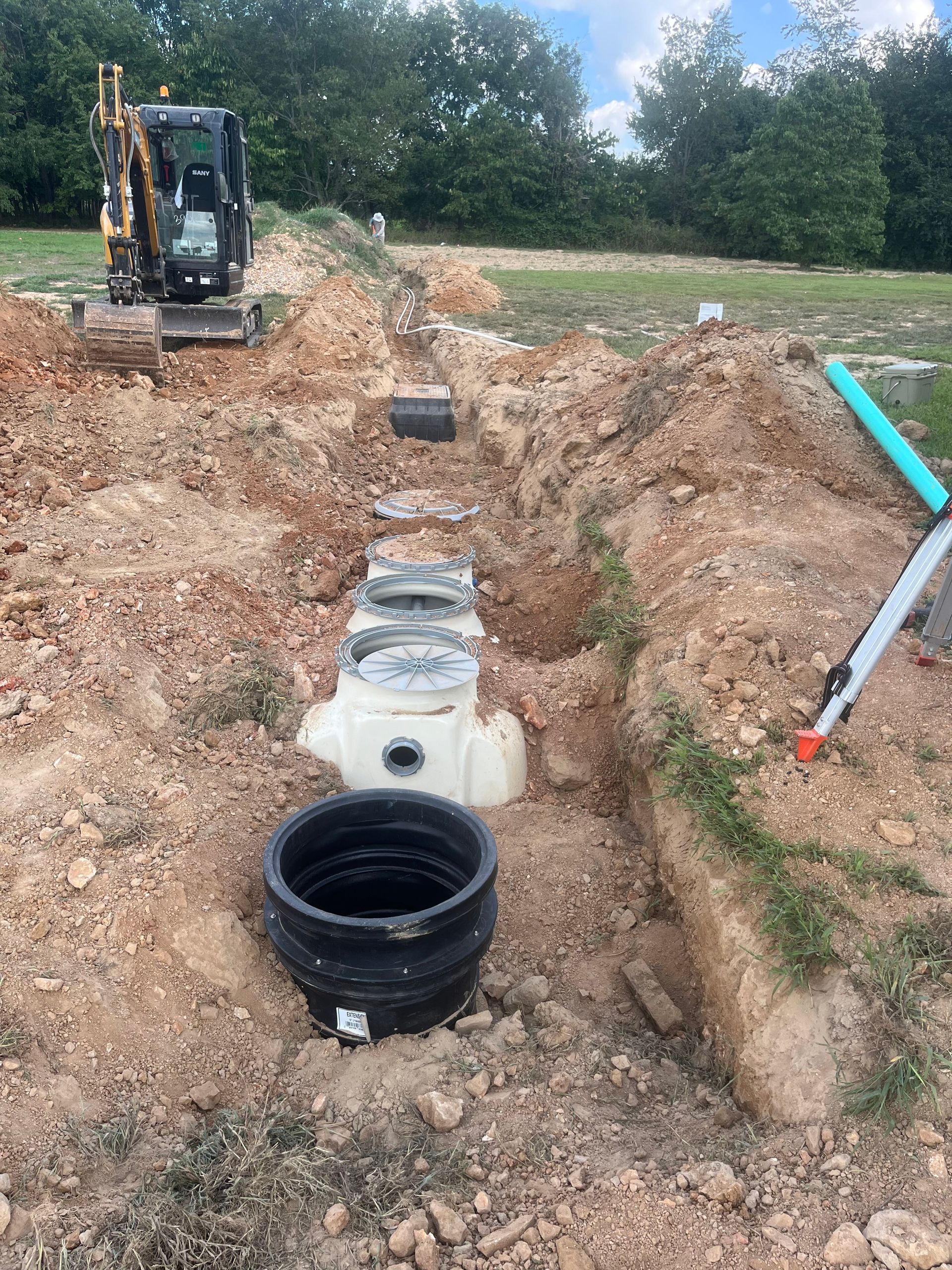 A septic tank is being installed in a dirt field with a bulldozer in the background.