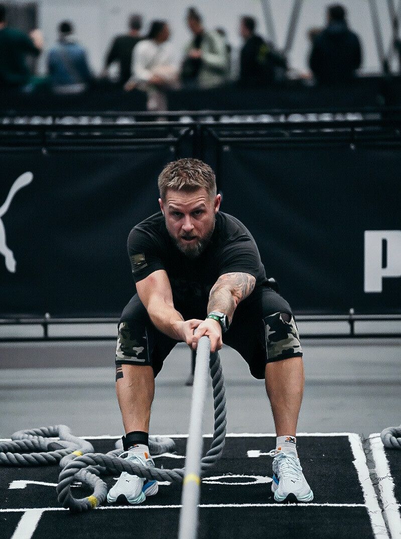 Ein Athlet umklammert Battle Ropes auf dem Hallenboden, konzentriert und in tiefer Trainingshaltung.