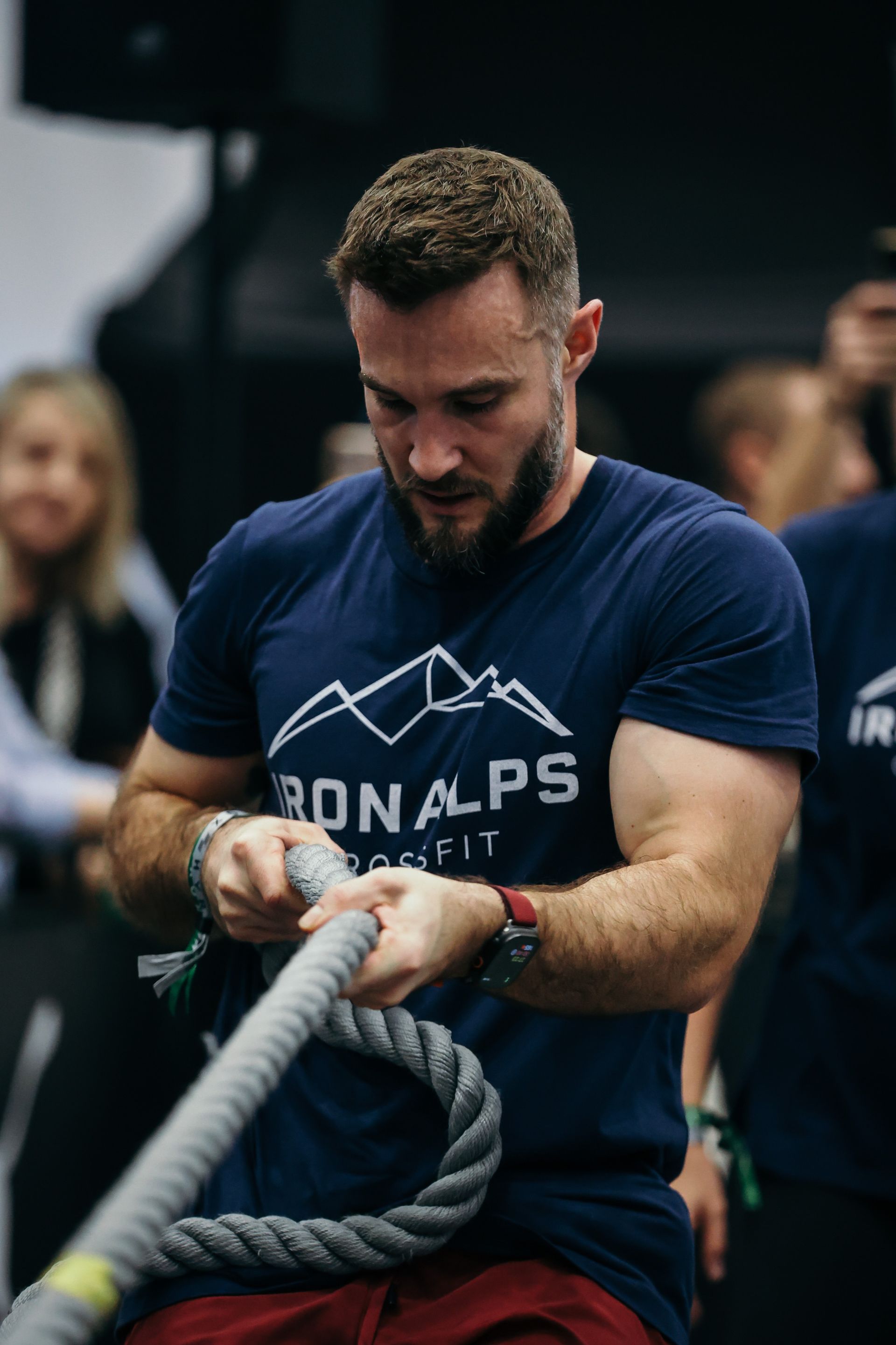 Mann im dunkelblauen Hemd umklammert ein Kampfseil während eines Indoor-Workout-Events