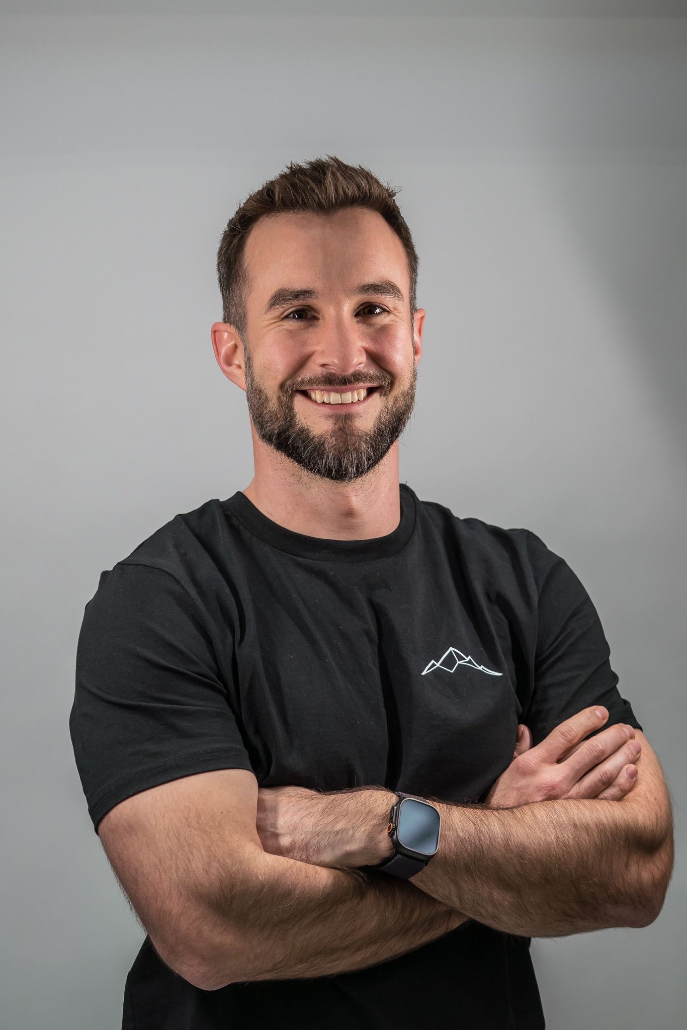 Lächelnder Mann in schwarzem T-Shirt mit verschränkten Armen vor grauem Hintergrund
