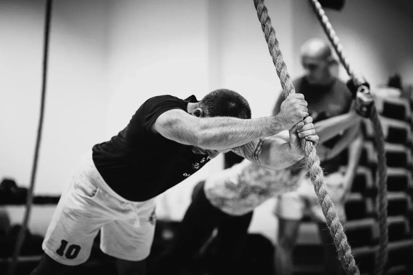 Ein Athlet in schwarzem Shirt und weißen Shorts beugt sich während eines Trainings nach vorn und hält ein Seil fest.