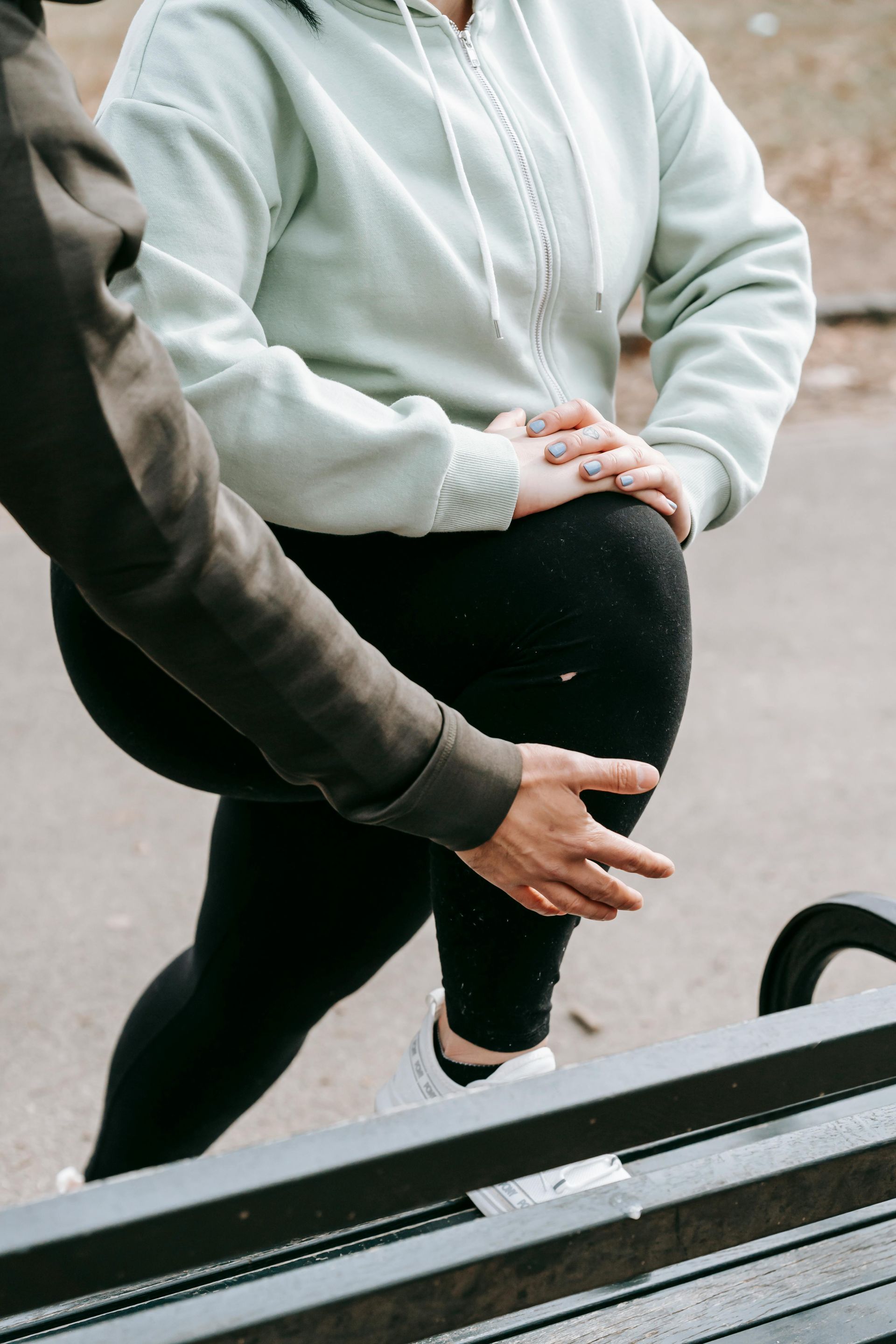 Zwei Personen joggen im Freien, eine von ihnen rückt ihren grauen Kapuzenpullover in der Nähe einer Bank zurecht.