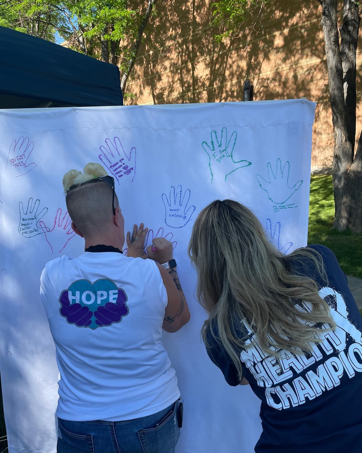 Two women are writing on a white board with their hands.