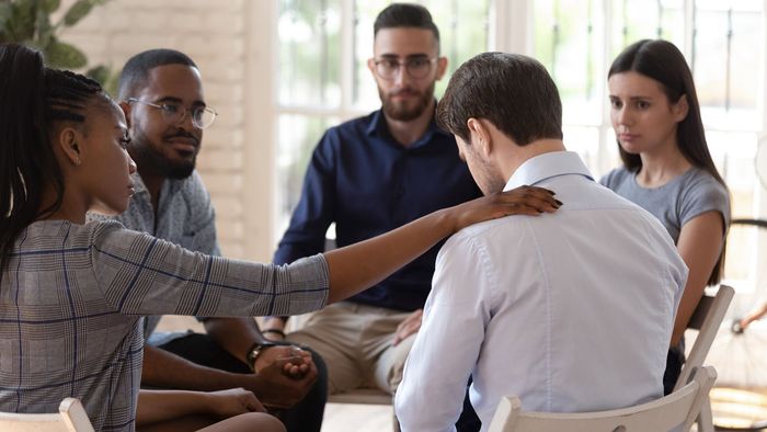 A group of people are sitting in a circle holding hands and talking to each other.