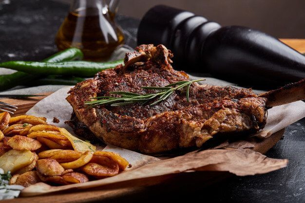 Gegrilltes Steak mit Kartoffeln, Rosmarin und Paprika auf einem Holzbrett.