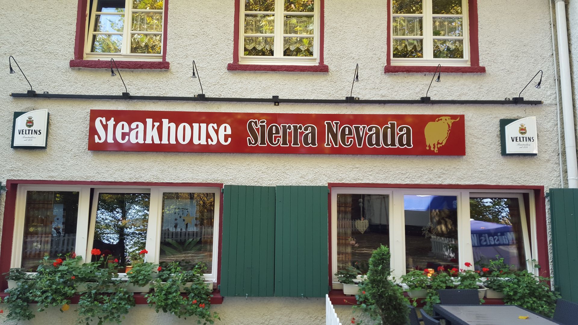 Das Steakhouse Sierra Nevada-Gebäude ist mit einem roten Schild, weißem Stuck und grünen Fensterläden ausgestattet.