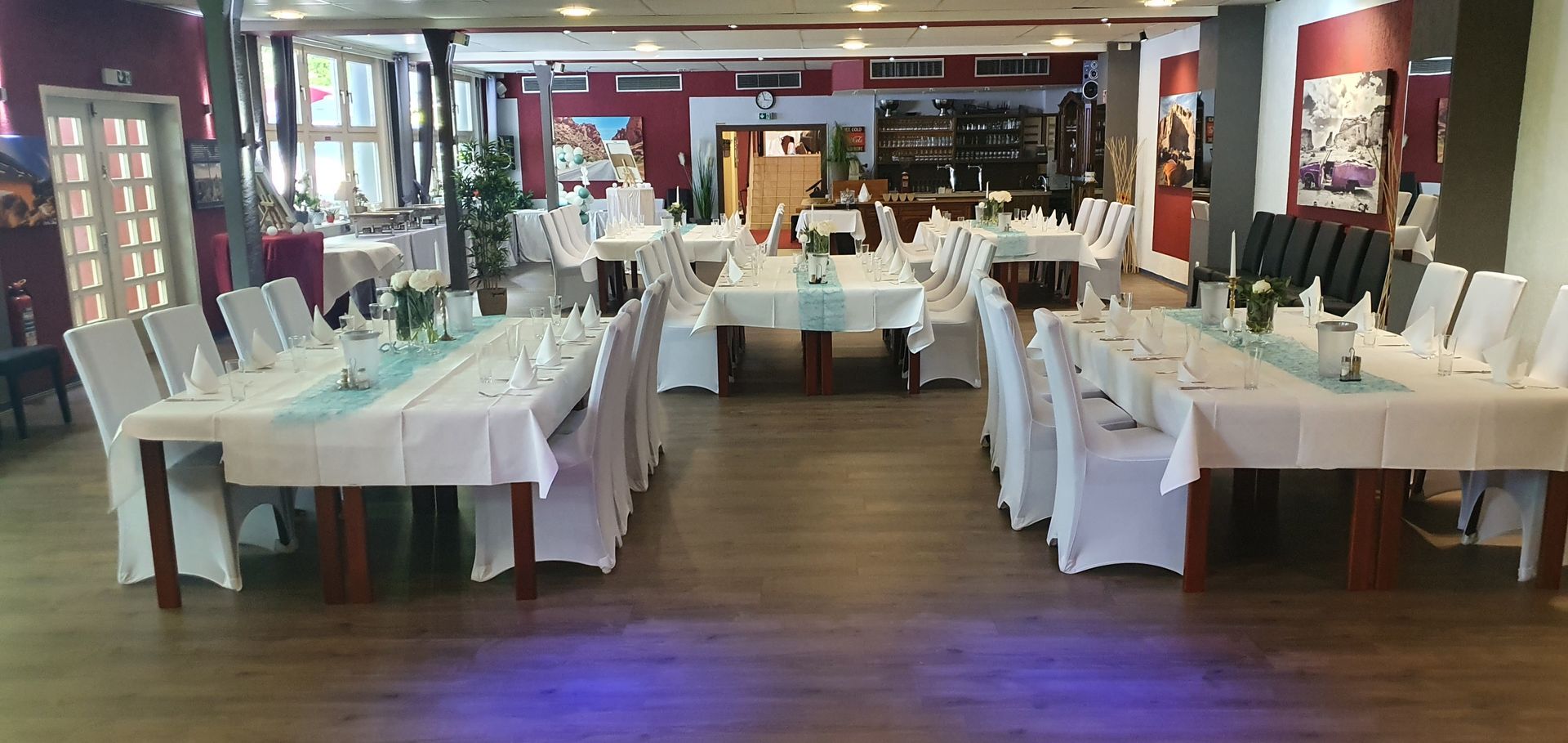 Restaurant-Speisesaal, gedeckte Tische, weiße Tischdecken, Stühle mit Hussen und blaue Tischläufer.