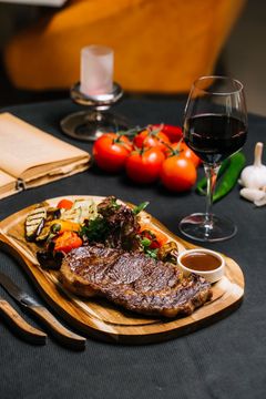 Steak-Dinner auf einem Holzbrett mit geröstetem Gemüse, Tomaten, Wein und einer Kerze.