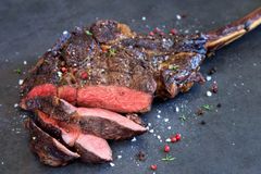 In Scheiben geschnittenes, scharf angebratenes Tomahawk-Steak mit sichtbarem rosa Kern, auf dunklem Untergrund.