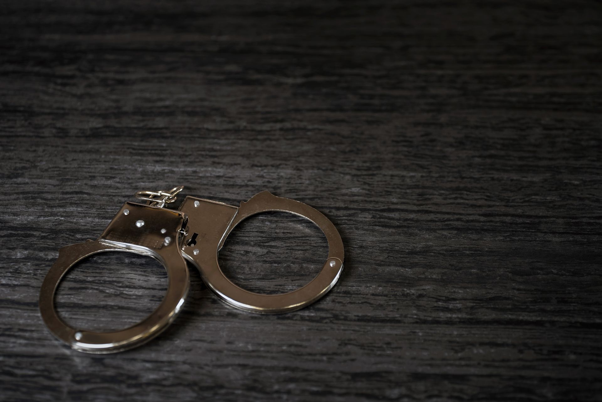 Silver handcuffs on a dark, textured surface. Silver handcuffs on a dark, textured surface.