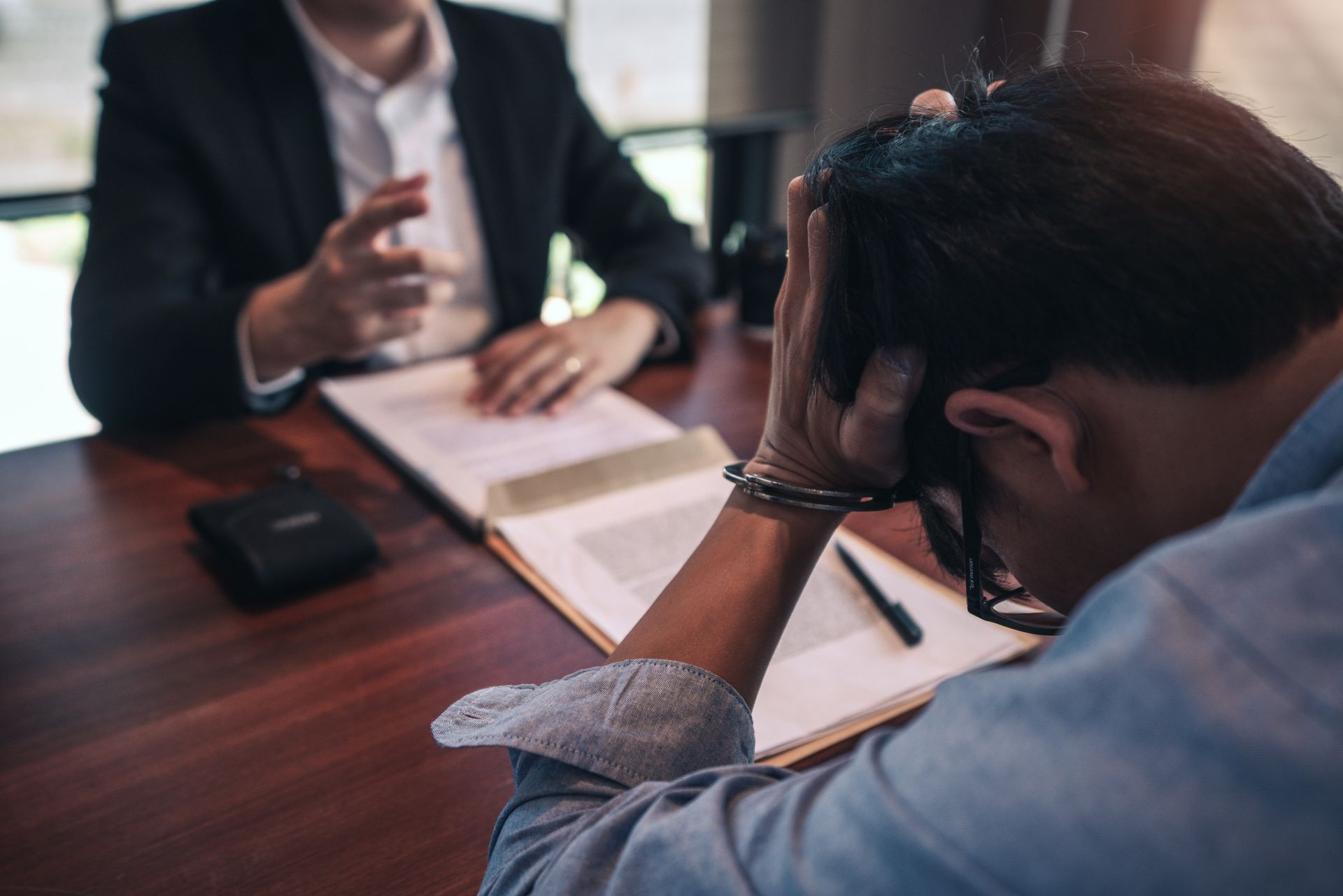 Man in handcuffs, head in hands, sits at a table with an attorney reviewing documents. Man in handcuffs, head in hands, sits at a table with an attorney reviewing documents.