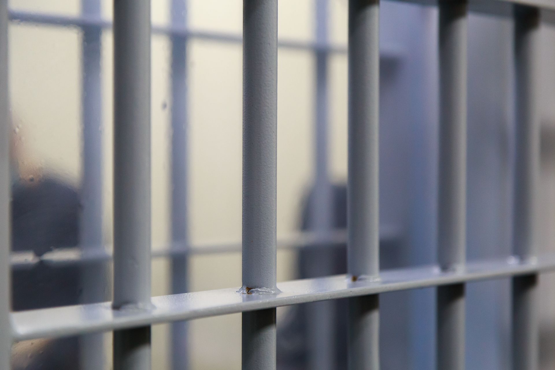 A close up of a prison cell with bars and a person behind them.