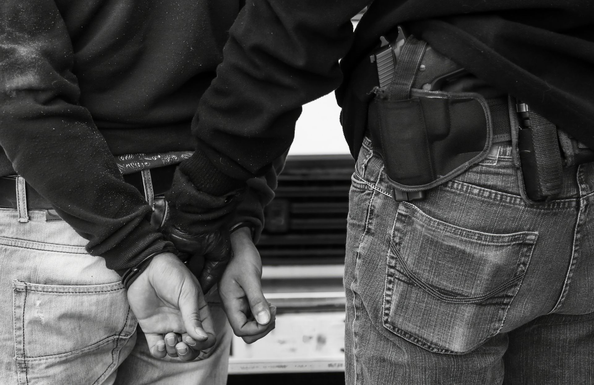 Person in handcuffs, being guarded by a person with a holstered gun. Person in handcuffs, being guarded by a person with a holstered gun.