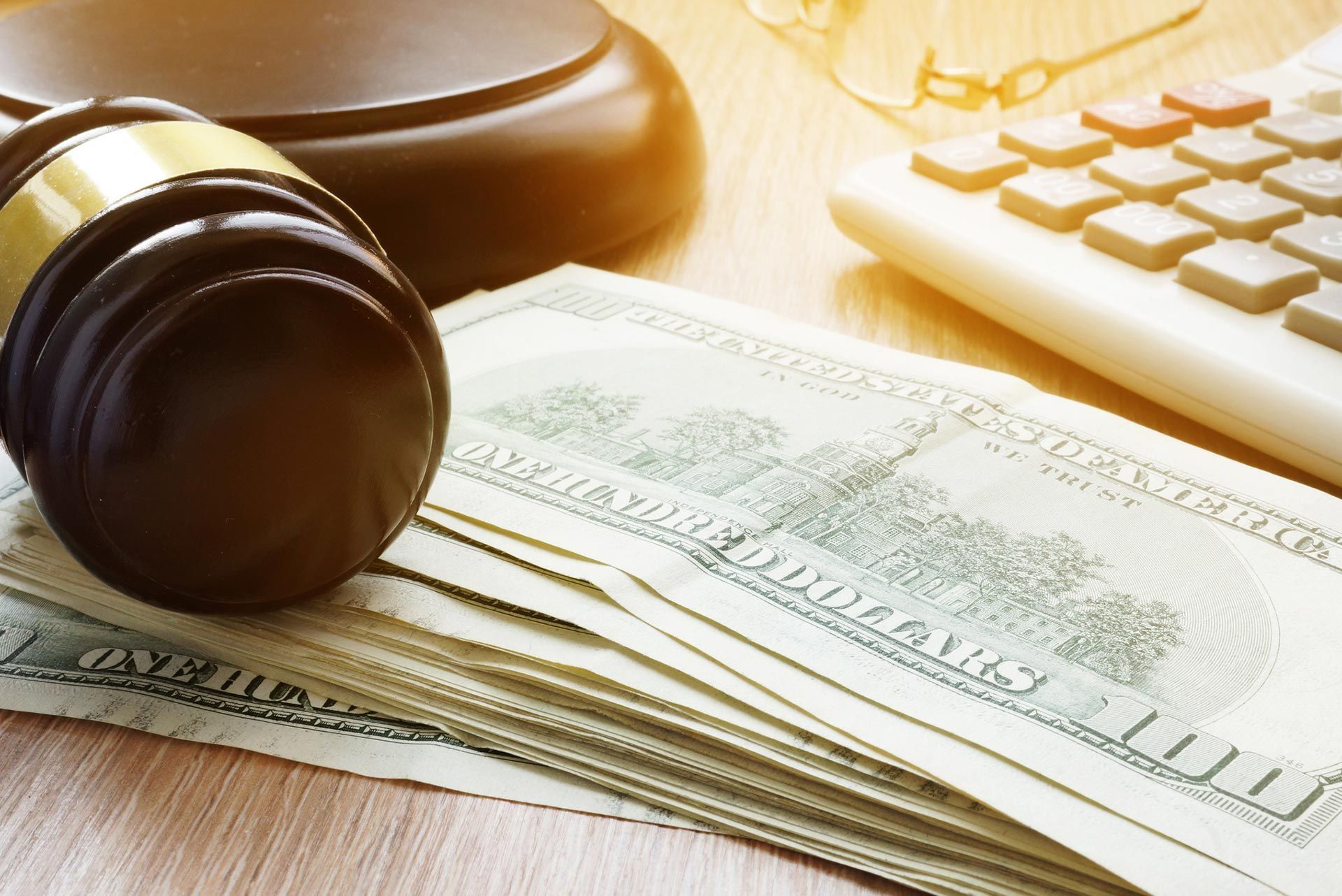 A judge 's gavel is sitting on top of a stack of money next to a calculator. A judge 's gavel is sitting on top of a stack of money next to a calculator.