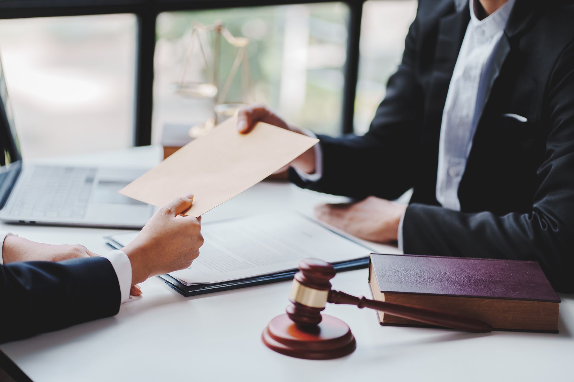 Two people in suits exchanging documents at a desk with a gavel and law book.