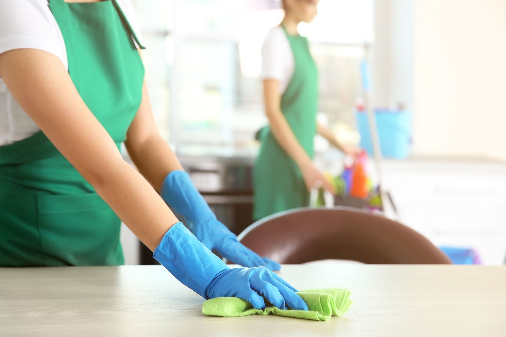 A woman wearing blue gloves is cleaning a table with a cloth.