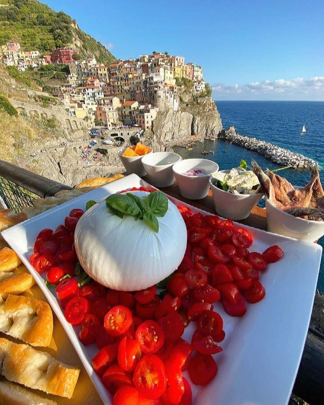 A plate of food with tomatoes and mozzarella on a table with a view of the ocean.
