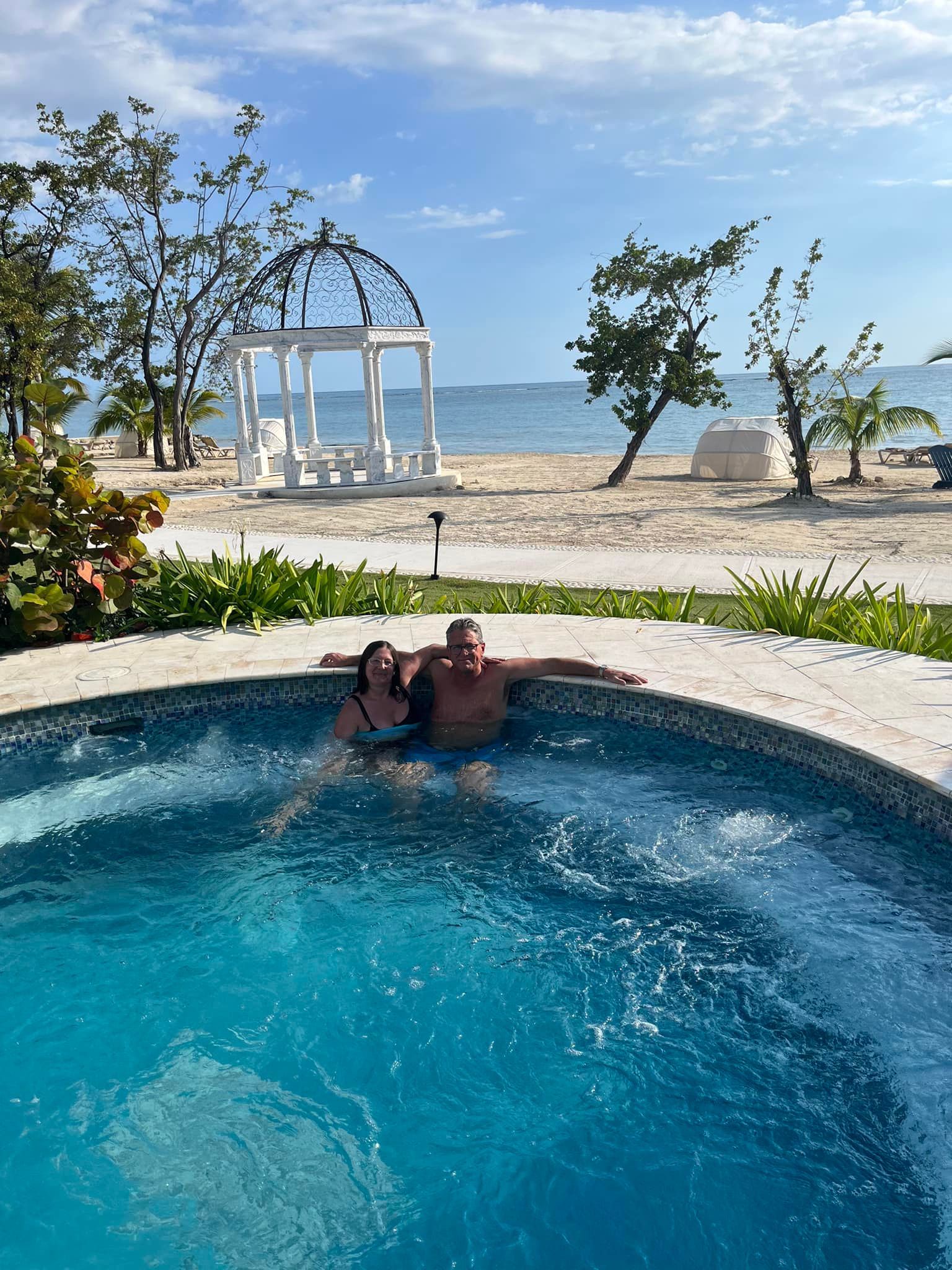 A man and a woman are sitting in a hot tub on the beach.