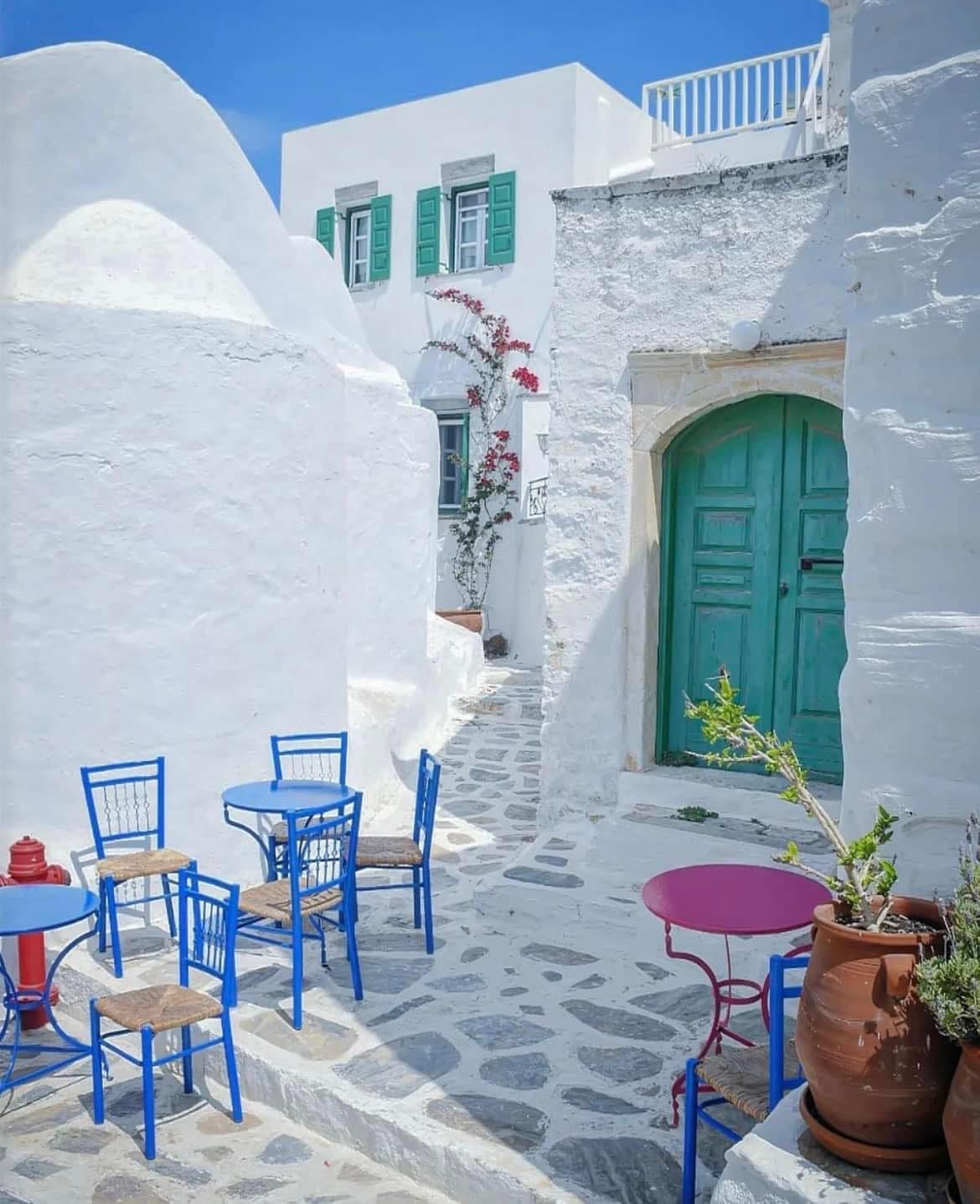 A white building with blue chairs and tables in front of it