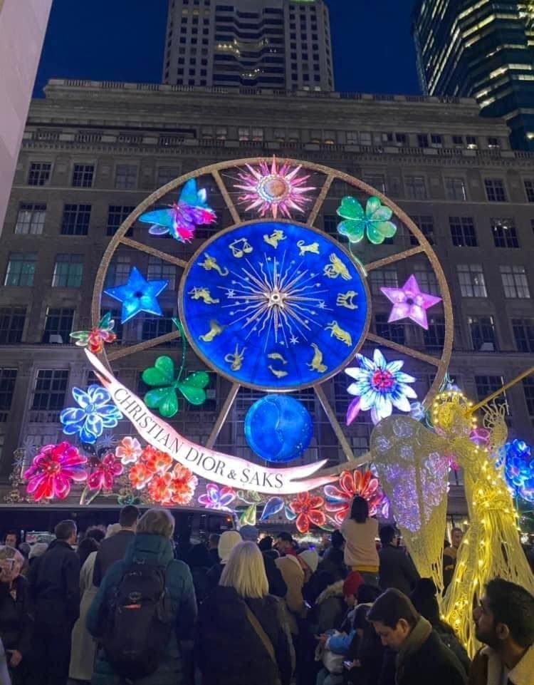 A crowd of people are gathered in front of a ferris wheel that says christine prors & saks