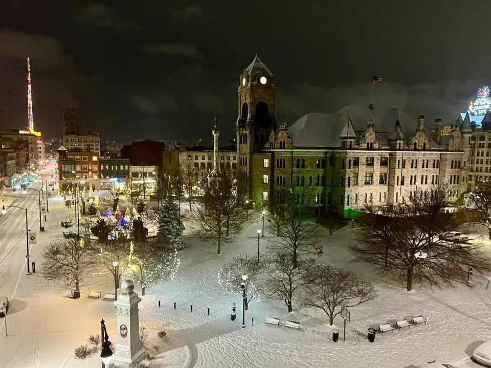 An aerial view of a snowy city at night with a clock tower in the background.