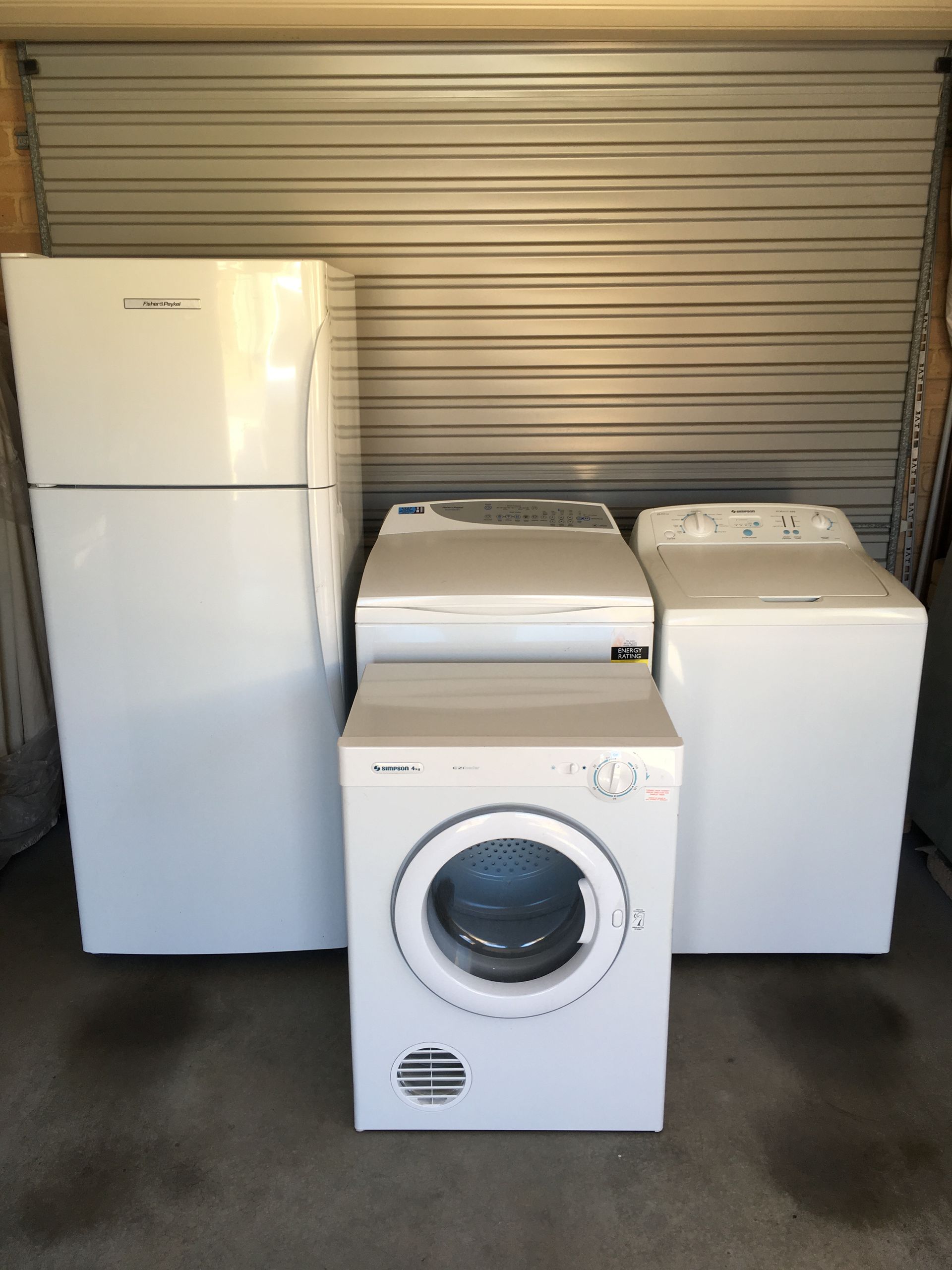 White refrigerator, washing machine, dryer, and top-load washer against a metal garage door — A.S.A.P. Appliance Service & Sales in Toukley, NSW