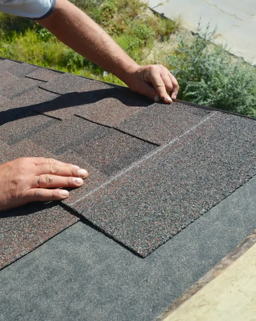 A man is standing on top of a roof holding a piece of shingles.